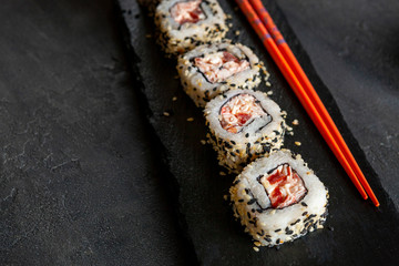 Japanese crab meat mousse sushi on stone board with chopsticks. Top view, close up on black concrete background.