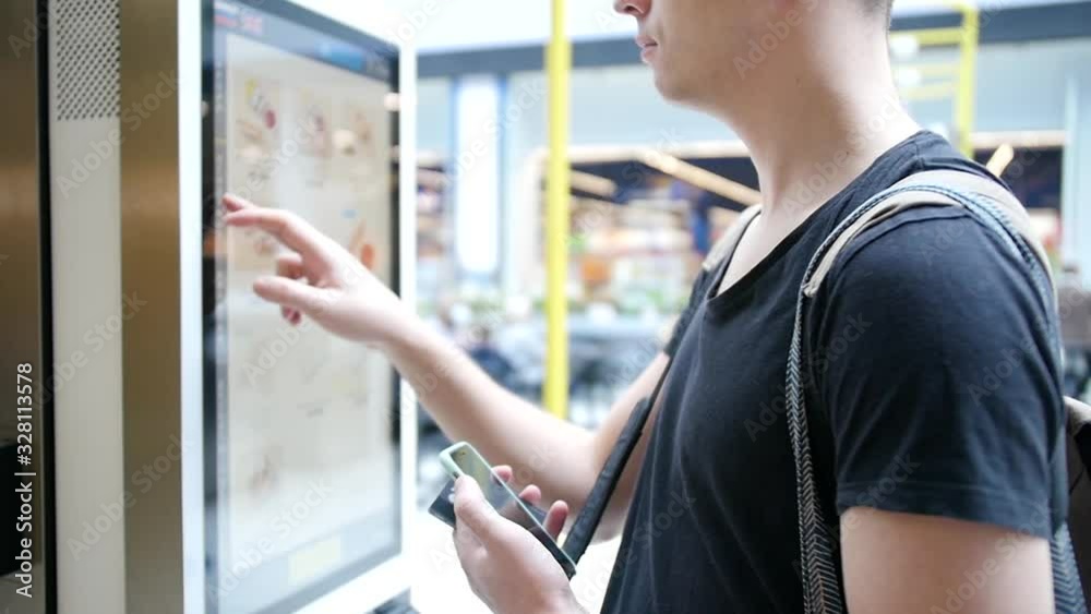 Wall mural young man makes an order using a digital screen. modern food ordering technology through a special s