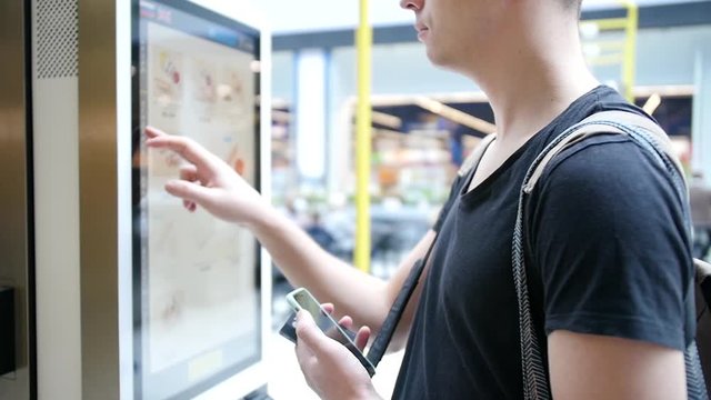 Young man makes an order using a digital screen. Modern food ordering technology through a special service without operators