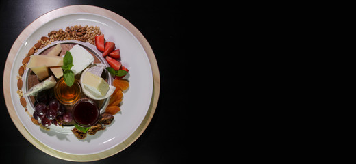 Cheese plate.Isolated on a black background.Copy space.Camembert cheese, Parmesan, blue cheese served with grapes, jam, figs, honey, strawberries, dried apricots and nuts on a white plate.
