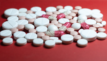 Heap of white pills, tablets, capsules on red background. Drug prescription for treatment medication health care concept wth copy space.