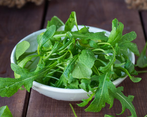 A white plate with a freshly picked arugula salad stands on a wooden table
