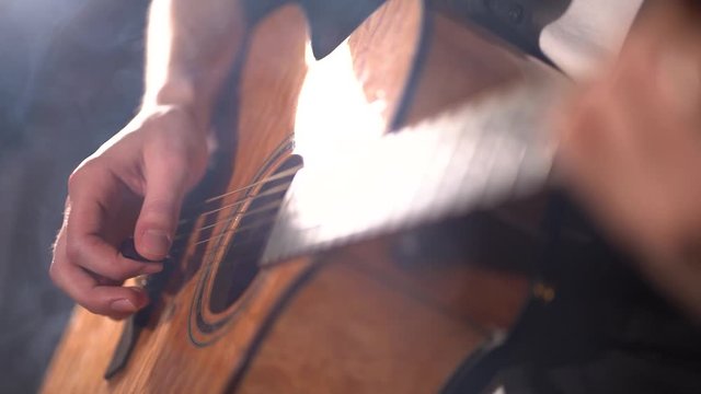 Slow motion closeup of a person strumming a guitar in a dark room while smoking