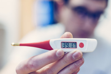 Flu and corona concept: Man is holding a fever thermometer in his hand, close up