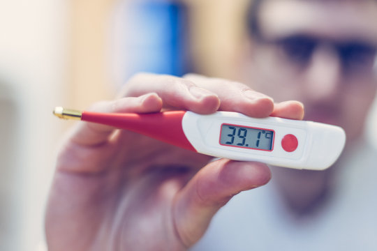 Flu and corona concept: Man is holding a fever thermometer in his hand, close up