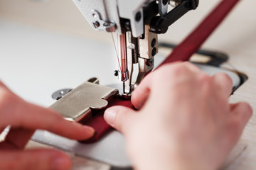 The hands of a master and the needle of a leather product sewing on a sewing machine. Manual work, business.