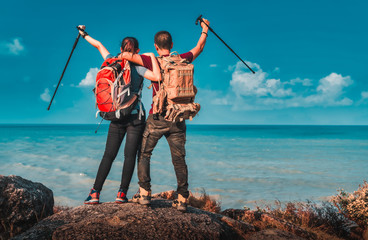 Young asian couple hikers climbing up on the peak of mountain near ocean. Two tourists with...