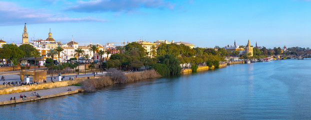 Fototapeta na wymiar Panoramic view of the waterfront of the Guadalquivir River in Seville, Andalusia, Spain. On a warm winter evening, people relax and stroll along the waterfront.