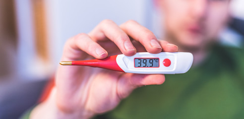 Flu and corona concept: Man is holding a fever thermometer in his hand, close up