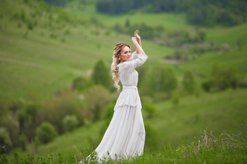 Fototapeta na wymiar the bride walks in the field against the backdrop of the mountain