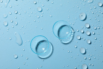 Contact lenses on blue background with water drops, close up