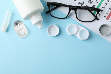 Glasses, contact lenses and eye test chart on blue background, top view