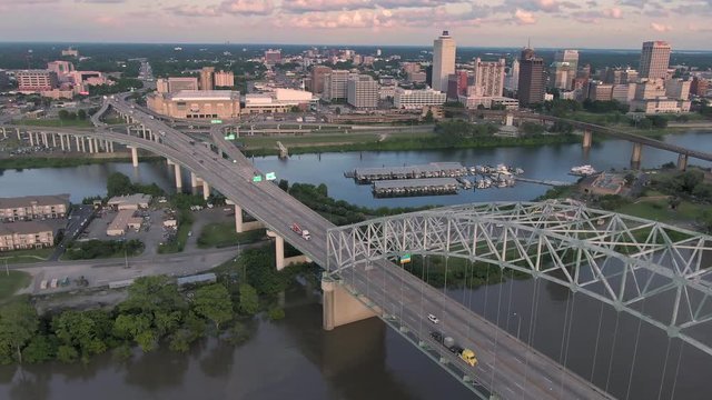 Aerial flying over traffic on the Hernando de Soto Bridge that crosses the Mississippi River at sunset. In the background is downtown Memphis, Tennessee, USA