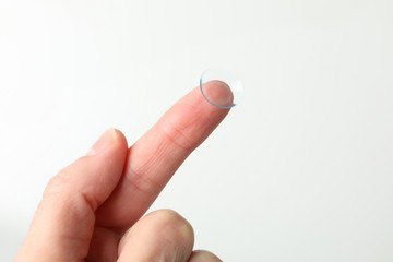 Female hand holds contact lens on white background, close up