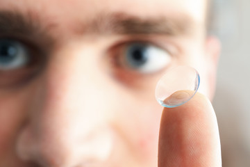 Man with blue eyes and contact lens on finger, close up