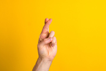 hoping for the best. close up hand with fingers crossed against yellow background with copy space