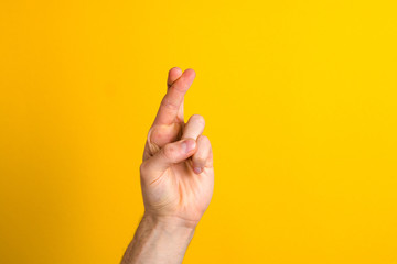 hoping for the best. close up hand with fingers crossed against yellow background with copy space