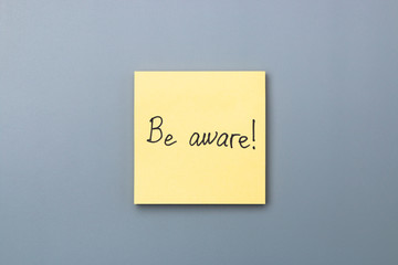 be aware on yellow sticky note over a grey background. april fools day