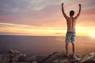 Man with raised arms standing on a cliff over the sea