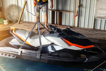 Senior man launching or lifting modern fast jetski hanged on strpas with wire hoist rail crane for...