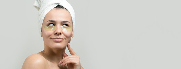 Young beautiful girl in a white towel on his head wears collagen gel patches under her eyes. Mask under eyes treatment face.