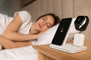 Smartphone, watch, earphones charging on wireless pad and sleeping woman in room © New Africa