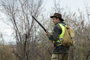 Fototapeta premium Hunting period, autumn season open. A hunter with a gun in his hands in hunting clothes in the autumn forest in search of a trophy. A man stands with weapons and hunting dogs tracking down the game.