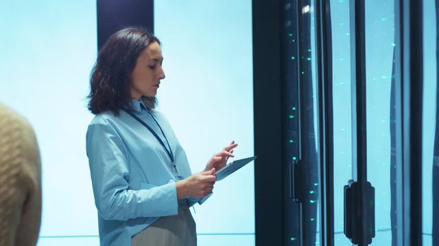 IT woman engineer doing cloud-based diagnostics with digital tablet visually inspecting active server cabinet racks collaborating in team for maintenance. Data center.