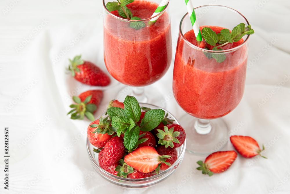 Wall mural two glasses of fresh strawberry smoothie and a bowl of ripe strawberries on the white background.