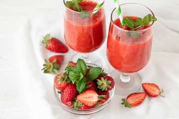 Two glasses of fresh strawberry smoothie and a bowl of ripe strawberries on the white background.