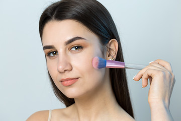 Close-up of a young girl in a light top on a white background making a facial make-up. A pretty...