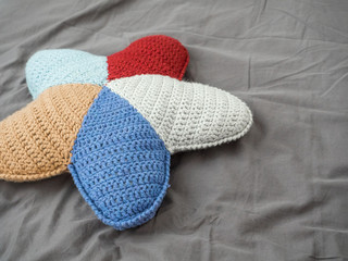 Closeup hand made multicolored yarn knitted pillow in the shape of a starfish on a gray background
