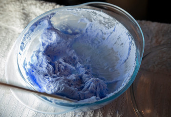  Hair dye product. Bleach for hair. Bowl with peroxide and brush, closeup on a purple background. 