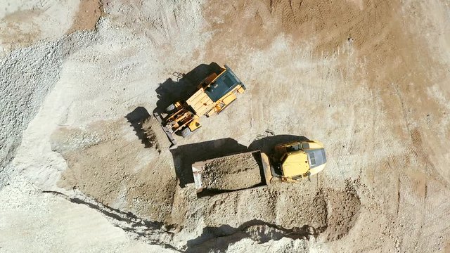 Bucket loader loading Gravel onto an Articulated hauler Truck trailer at a large construction site, Top down aerial view.