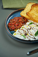 Tasty strachatella cheese with tomato salsa and croutons in a blue plate on a wooden background. Italian Cuisine. Breakfast food, close up, selective focus, vertical
