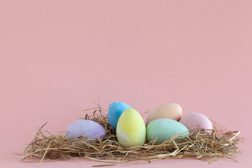 Pastell-farbene Eier im Strohnest auf pinkfarbenem Hintergrund