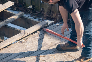 Man Dismantling an Old Wooden Deck with a Red Crowbar in a Backyard