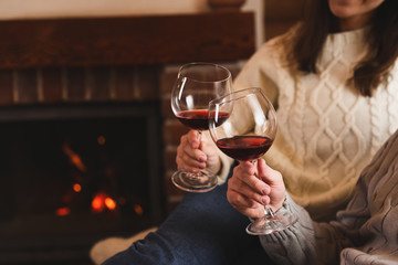 Lovely couple with glasses of wine resting near fireplace at home, closeup. Winter vacation - obrazy, fototapety, plakaty