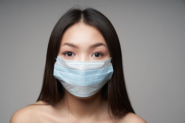 A young beautiful Asian woman in a medical mask, on an isolated gray background, looks directly at the camera. Concept of health,protection, prevention of bacterial infection 