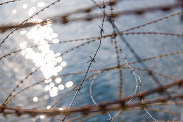 Rusty nato wire, rusty barbed wire, water in the background, border, abstract