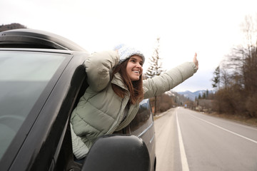 Happy woman leaning out of car window on road. Winter vacation