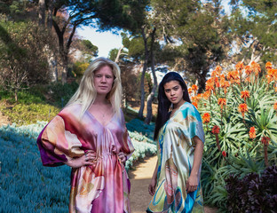 Young women, one is albino and another is Latin in nature with a hand-painted silk dress looking at the camera on a sunny day