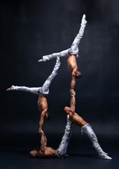 Four muscular man perform difficult acrobatic tricks on black studio 