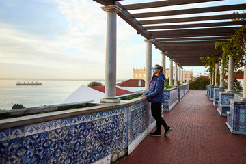 Fototapeta premium Beautiful women tourist looks at the red roofs of Lisbon from the viewpoint Miradouro de Santa Luzia