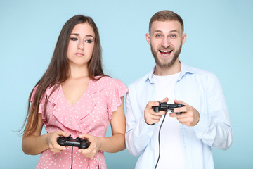 Happy young couple playing computer game with joysticks on blue background