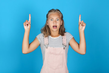 Portrait of young girl showing fingers up on blue background