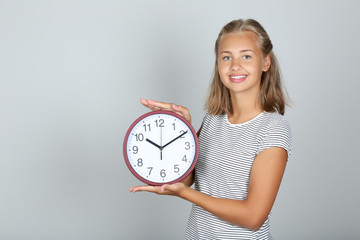 Young girl holding round clock on grey background
