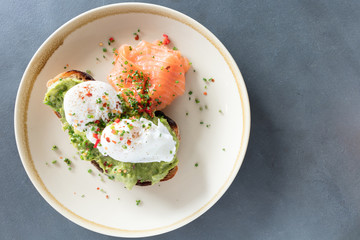 Poached eggs on top of smashed avocado on sourdough toast with smoked salmon. Healthy breakfast with plate on table. Top view.