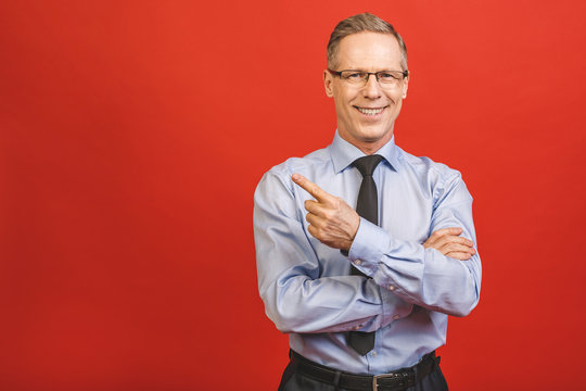 Follow me! Look here! Close up portrait of cheerful satisfied pleased qualified experienced joyful aged businessman pointing on empty blank place isolated on red background.
