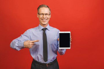 Senior aged middle aged man holding tablet with blank screen isolated over red background.